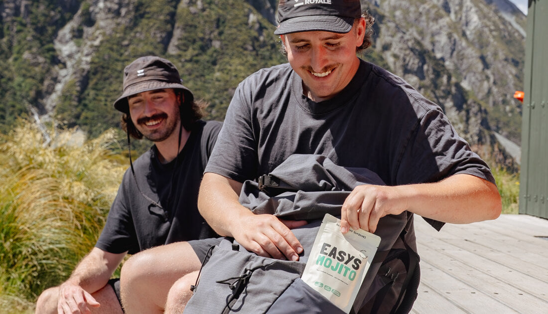 A hiker pulling an Easys cocktail pack out of their backpack in the backcountry, showcasing its lightweight and packable design for adventures.